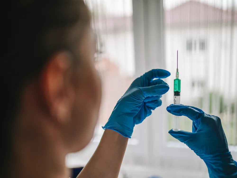 An over-the-shoulder shot of a woman, wearing blue gloves, preparing a syringe.