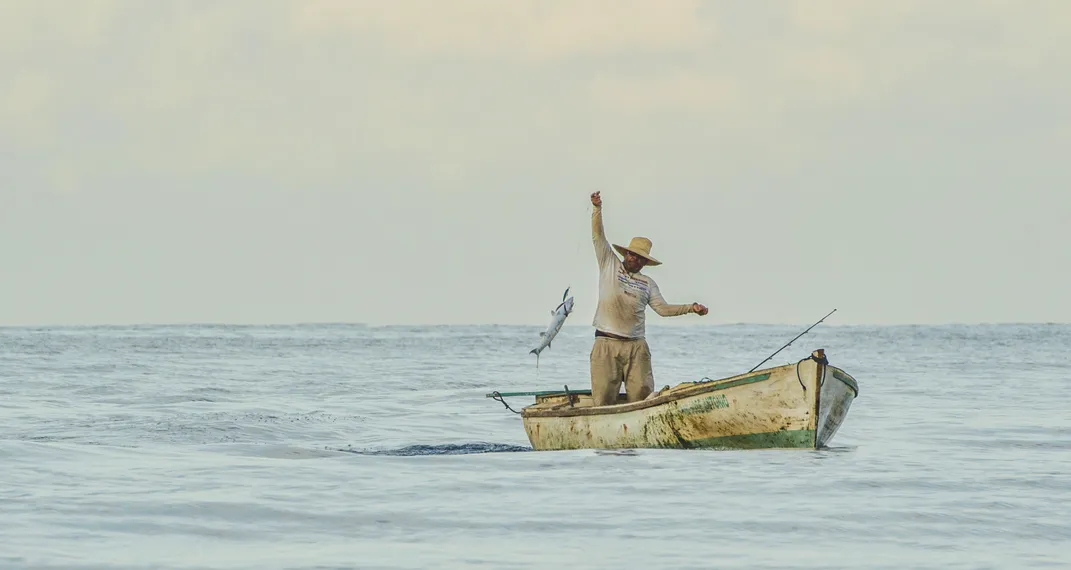 A person in a small boat hauls a fish out of the ocean.