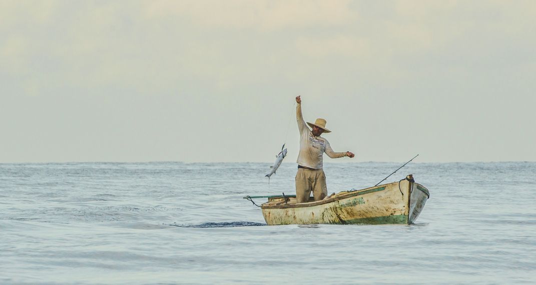 A person in a small boat hauls a fish out of the ocean.