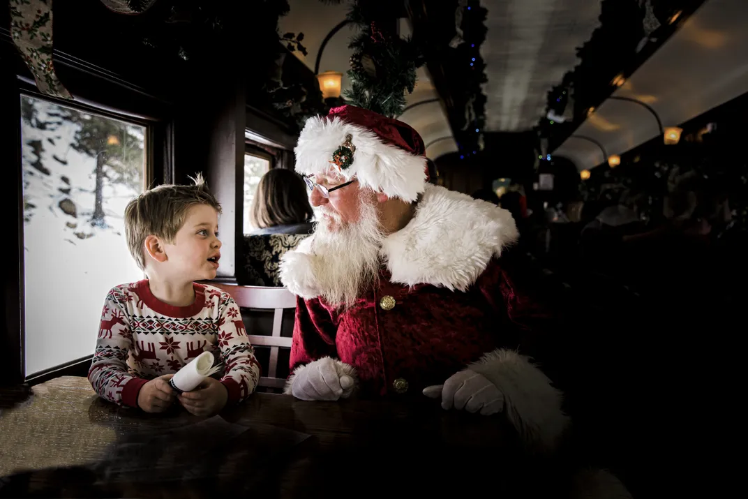 Santa Claus and a child sit together on a train.