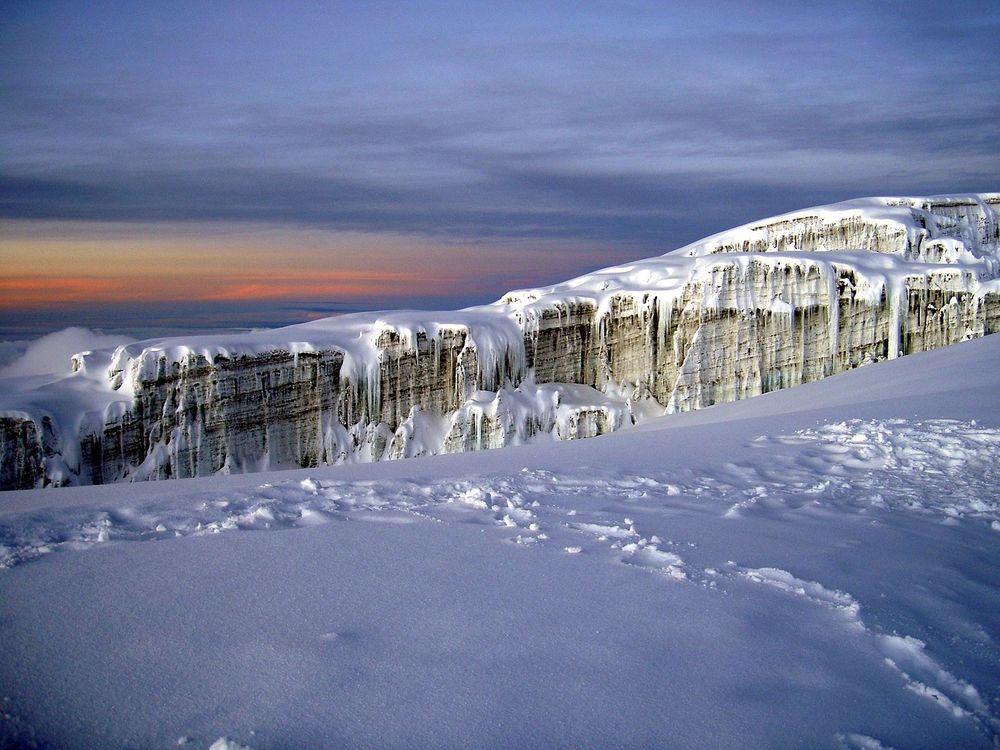 The face of a jagged white glacier on top of a snowy mountainside