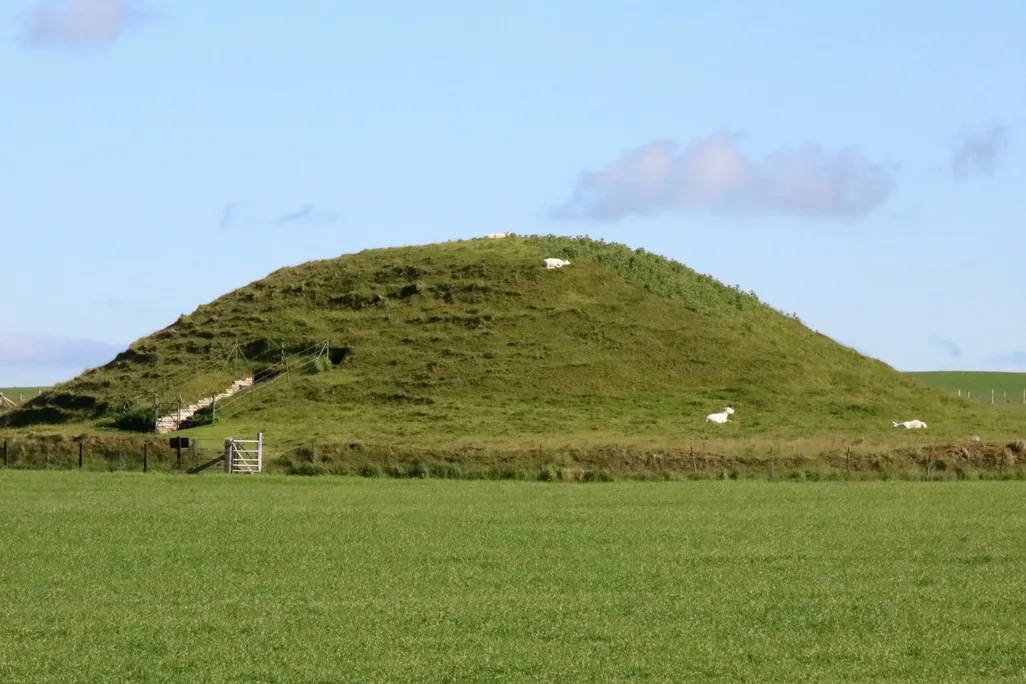 A large grassy mound with an entrance cut into the side, underneath a blue sky