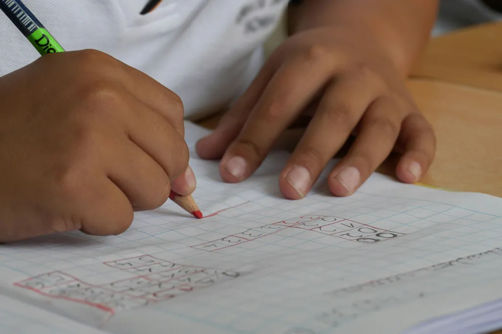 A close-up shot of a child writing on a piece of paper with their right hand