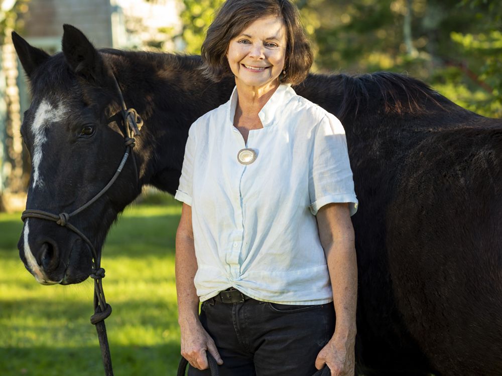 Image shows a woman wearing a white shirt standing with and holding the reins of a horse