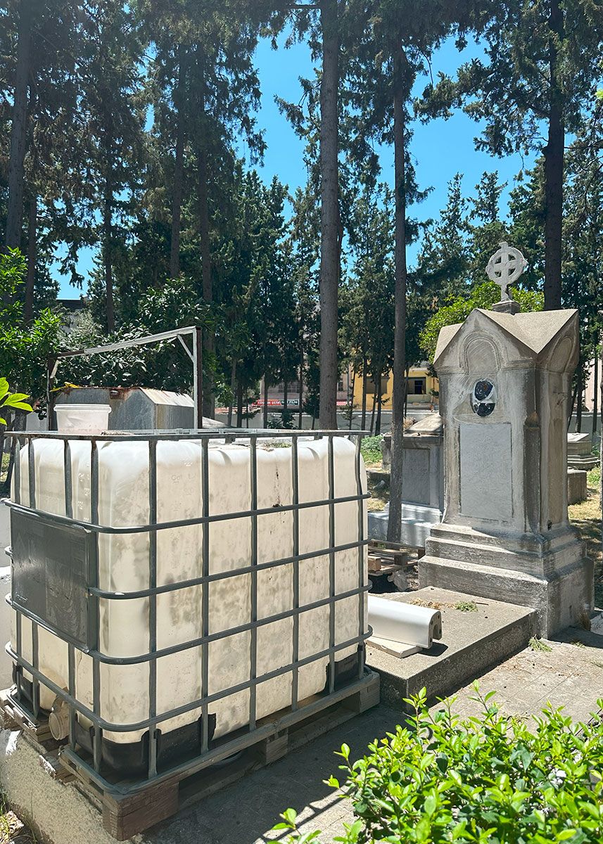 Among grave markers, a large white plastic tank in a wide metal cage.