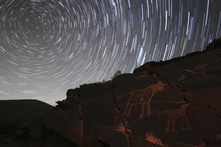 Depictions of catlike animals are visible on stones under a rotating, starry sky.

