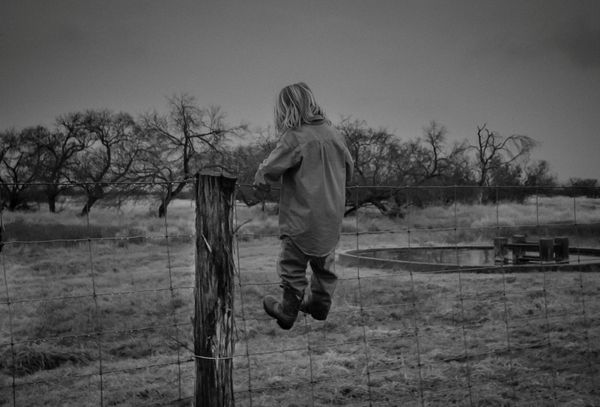 A young boy wanting to explore the brush country beyond the fence. thumbnail