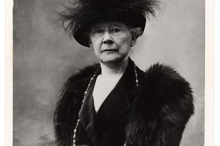 Black and white portrait of Mary Cassatt sitting in a chair wearing fur and a feathered hat.