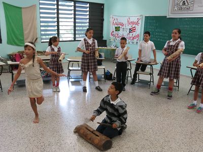 In this April 10, 2015 photo, Brayan Lopez, 9, plays a Taino wood drum while students perform a ceremonial dance in San Lorenzo, Puerto Rico. 