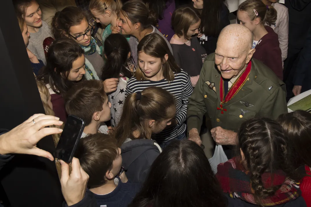 Elderly man in military dress uniform greets a crowd of small children