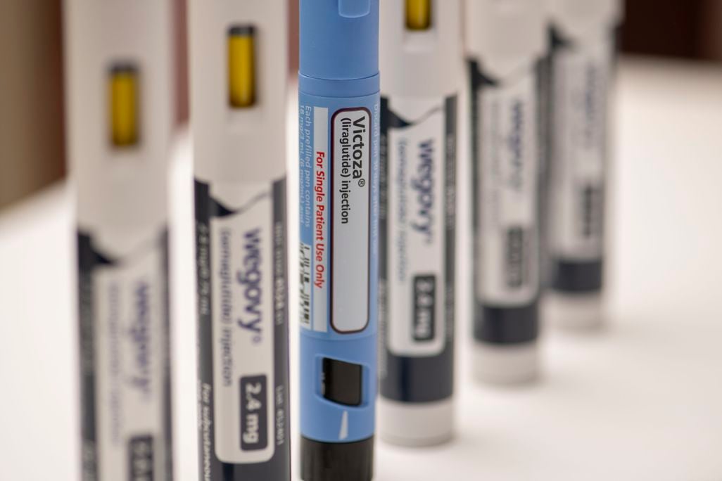 A blue Victoza pen stands in front of blurry, white Wegovy pens
