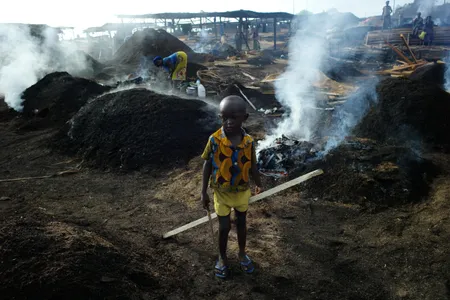 A child stands in the Côte d’Ivoire charcoal yard where his mother works.