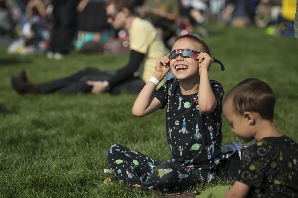 Little boy wearing eclipse glasses and smiling up toward the sky