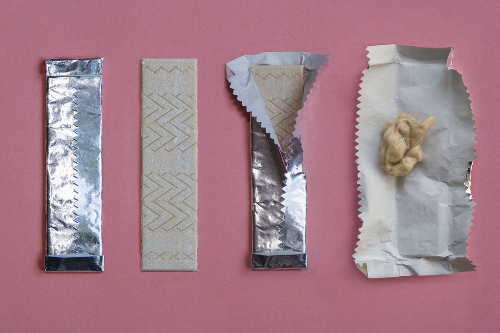 An image of a stick of gum shown in the stages of being used. Starting with unwrapping the stick of gum to ending with sticking the used piece in its foil wrapper. The sequence is shown against a pink background.