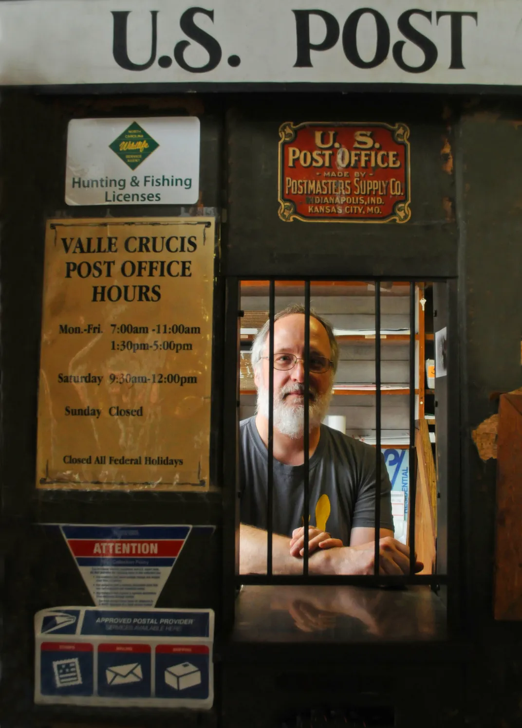 A man stands behind a post office window