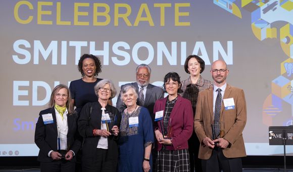 Group of Smithsonian Education awardees with leadership standing in front of a large screen that says "Celebrate Smithsonian Education"