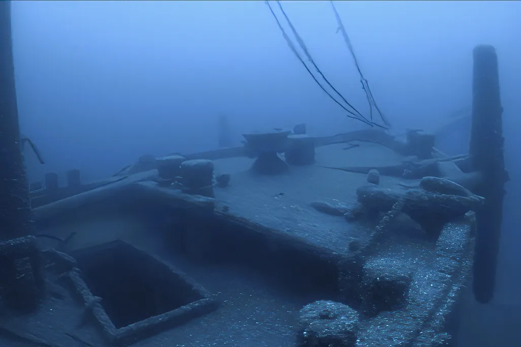 The deck of a wooden schooner vessel where the anchor is still visible near the bow