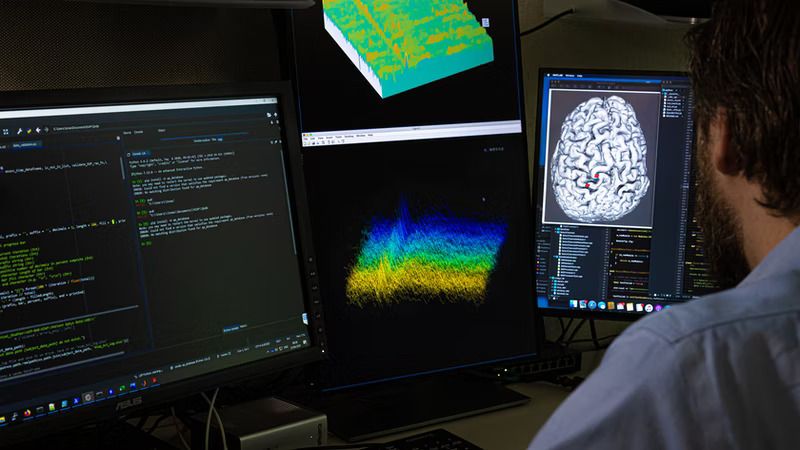 A person sitting in front of screens, one showing a brain