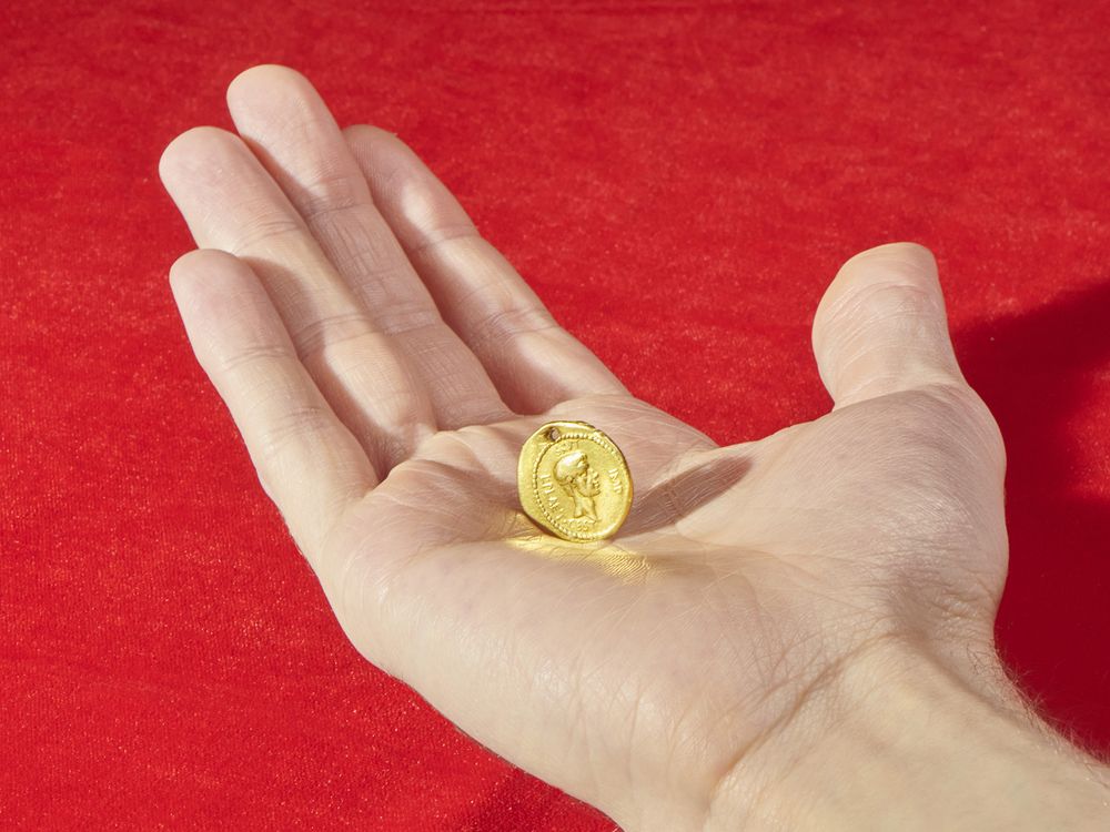 A white hand extends over a red background and holds the golden coin in their palm