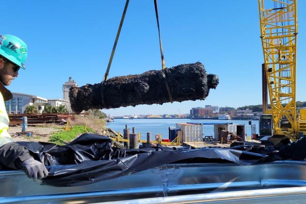 Worker in yellow safety vest working machinery that lifts rusted cannon from water