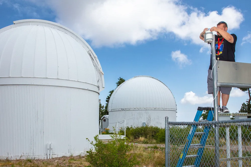 a man on a ladder outside several observatory buildings with domed roofs