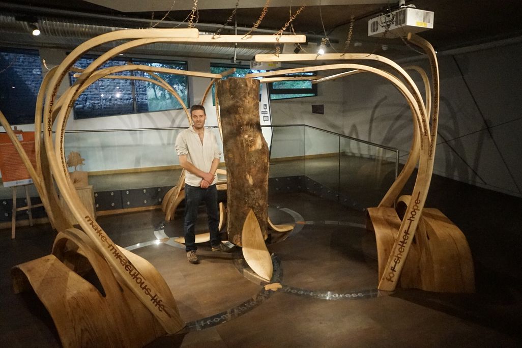 Man standing inside art installation next to tree trunk