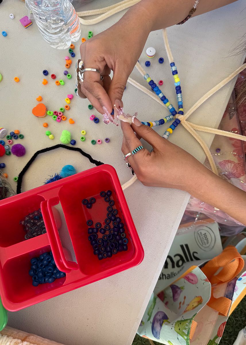 From above, two hands thread colorful plastic beads onto several connected strands of pipe cleaner.