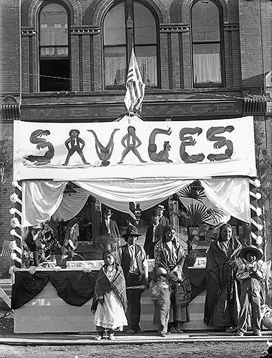 American Indians posed in front of a booth with sign advertising SAVAGES