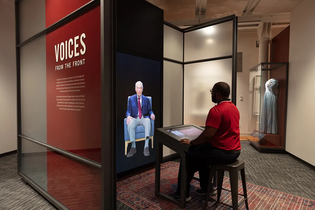 A visitor sits across from a video of a veteran on a screen