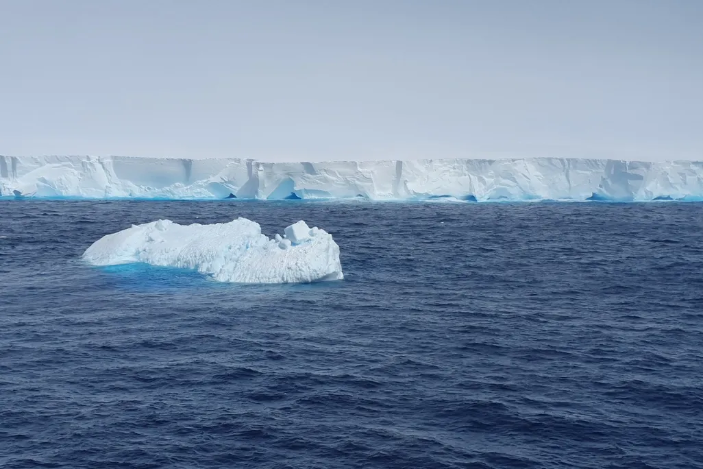 A small iceberg drifts in the ocean in front of a larger one