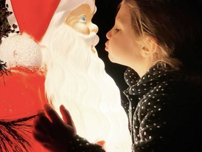A young girl puckers up to plant a kiss on a plastic Santa.

&nbsp;