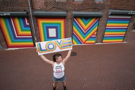 Lisa Marie Thalhammer holds her original LOVE poster with her mural in the background. 
