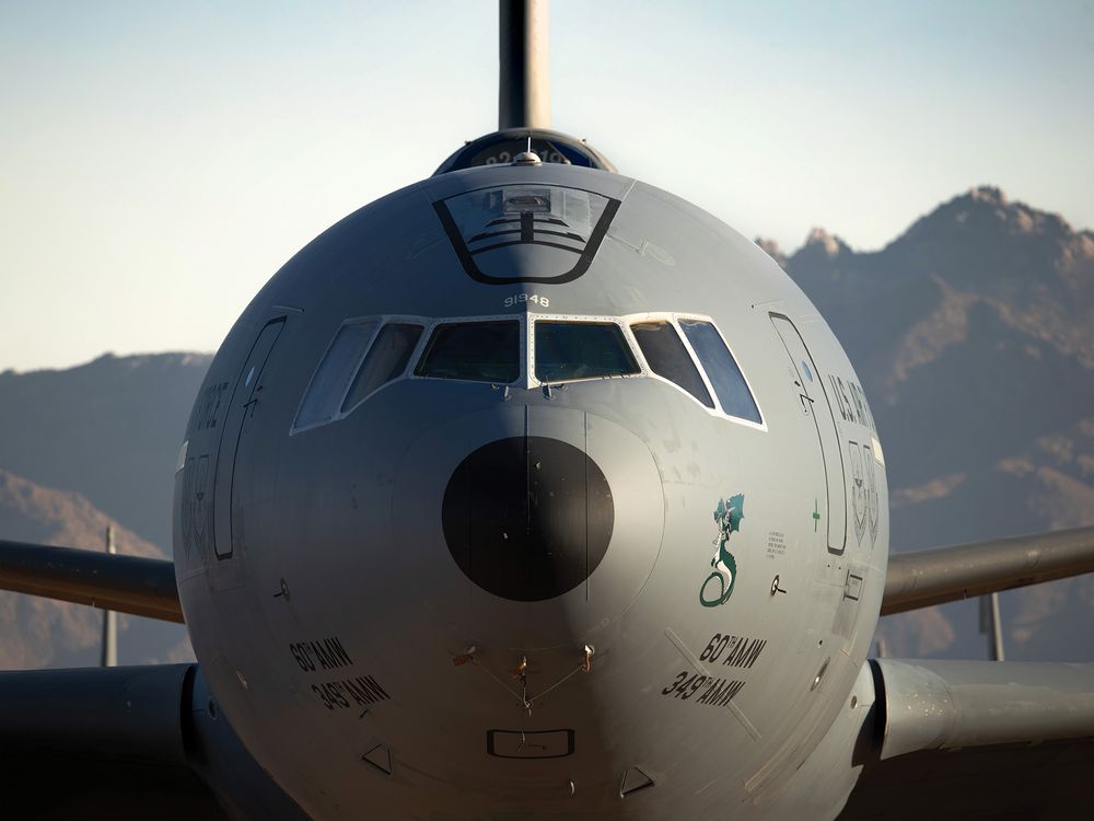 A close-up, head-on view of the nose and cockpit section of a gray U.S. Air Force KC-10 Extender aircraft parked in an aircraft boneyard, with mountains in the distant background.