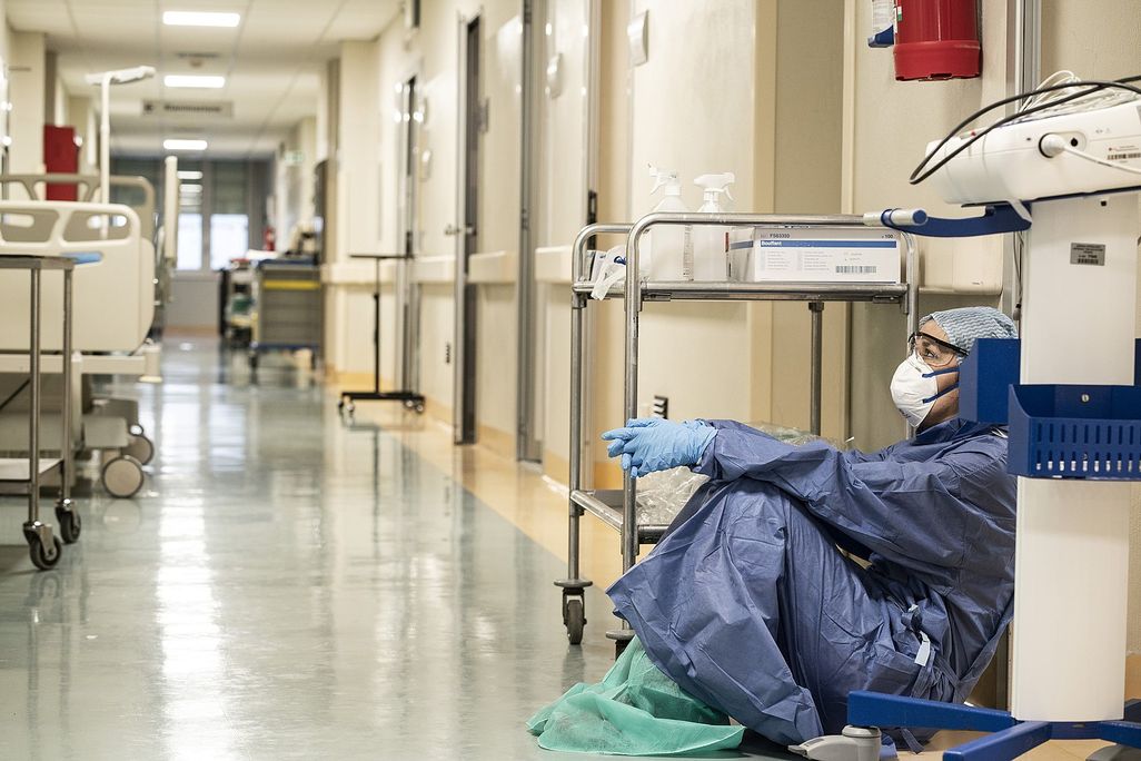 A female doctor wearing protective equipment sitting on the floor of a hospital hallway in Italy