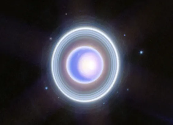 Uranus shown with its rings, appearing a blue-purple-white. It is surrounded by nine moons that are pinpricks of light