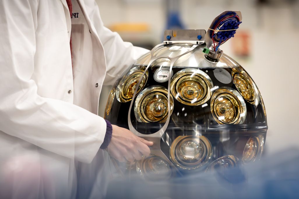 a scientist's hands hold onto a large metal sphere with many dials