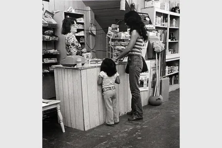 A woman and child stand at a shop counter facing a woman behind the register.