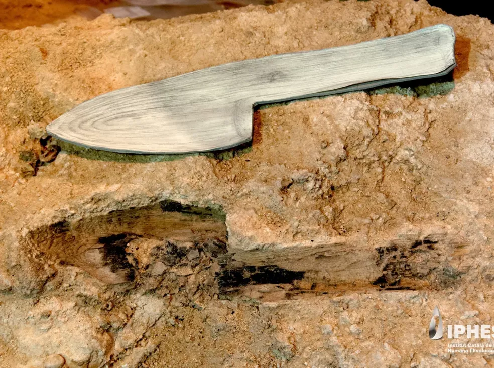 knife-shaped object next to a hole in the dirt that's the same shape