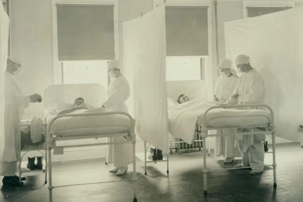 A black and white photograph of patients being treated by nurses during the 1918 influenza pandemic in a ward