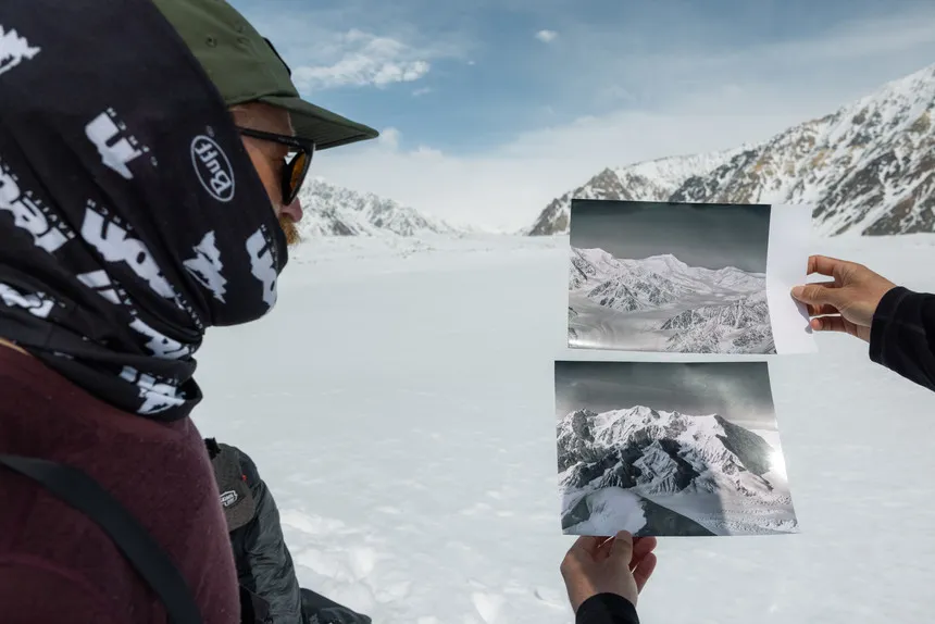 A person compares two photographs to a snowy mountainous landscape