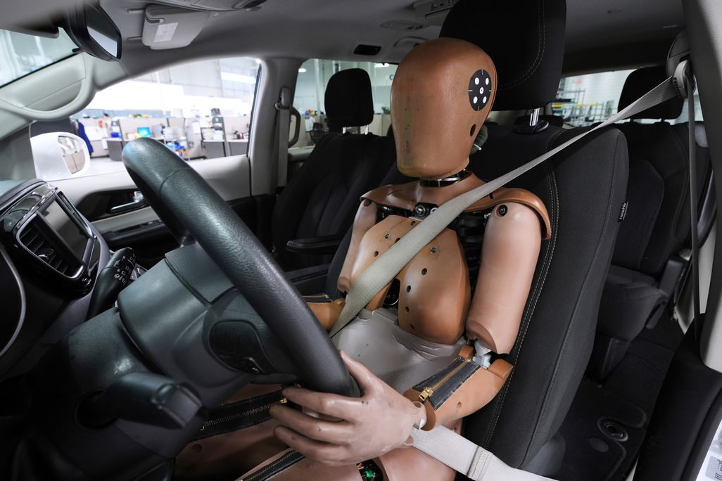 A crash test dummy in a car with the seat belt buckled