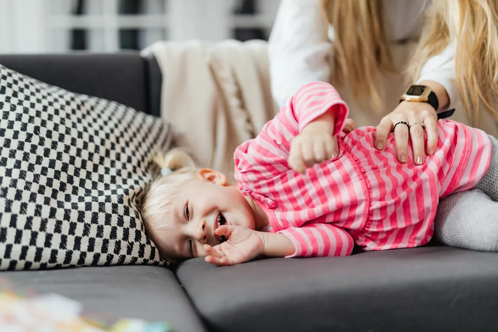 A little girl on a couch being tickled on her side