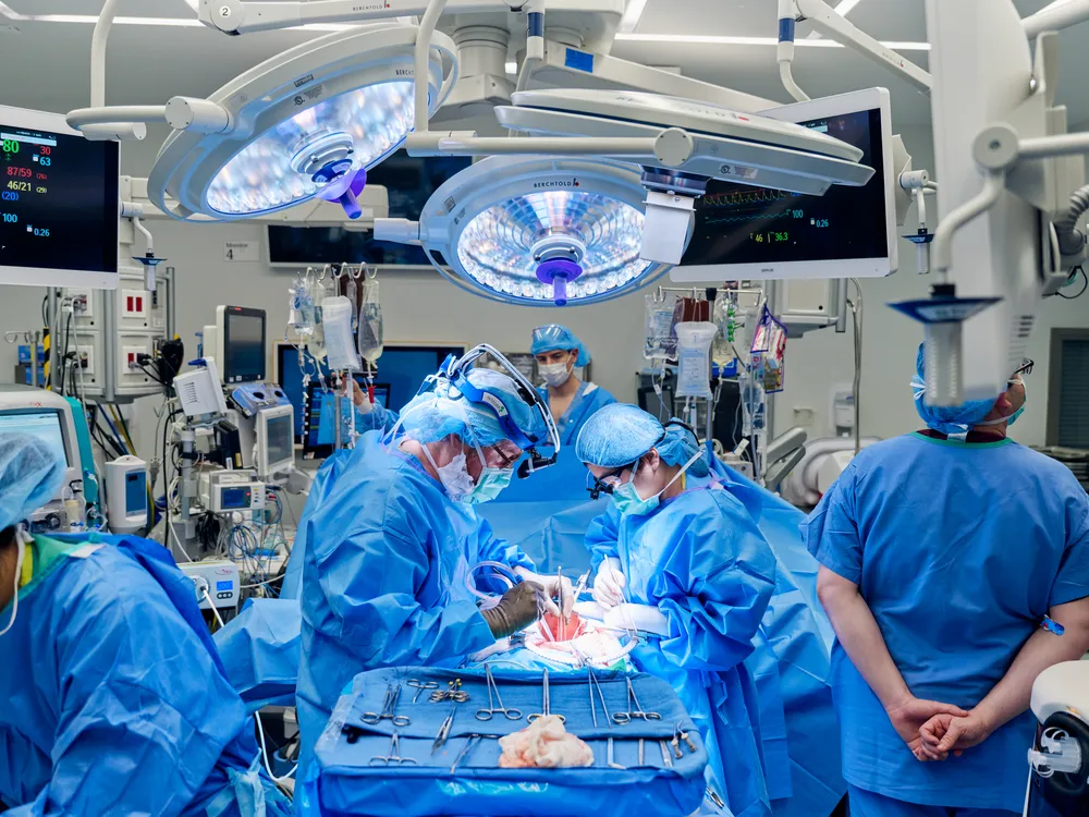 Surgeons in blue scrubs gathered around a patient on an operating table