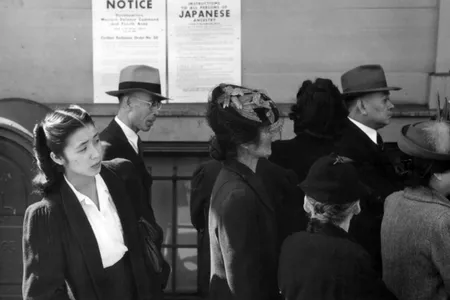 Japanese Americans stand in front of a poster with internment orders.