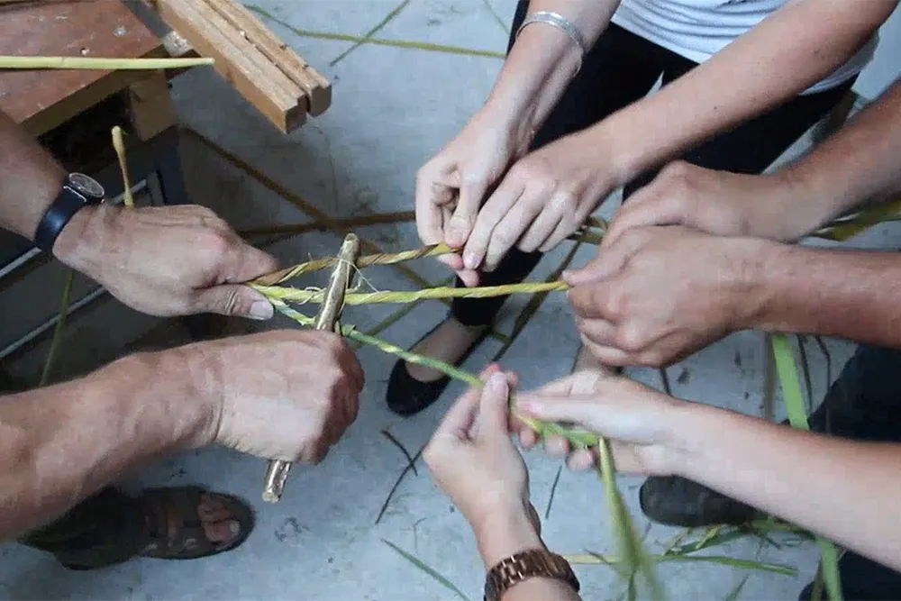 four pairs of hands spin cattail fibers through a replica of a Stone Age perforated baton