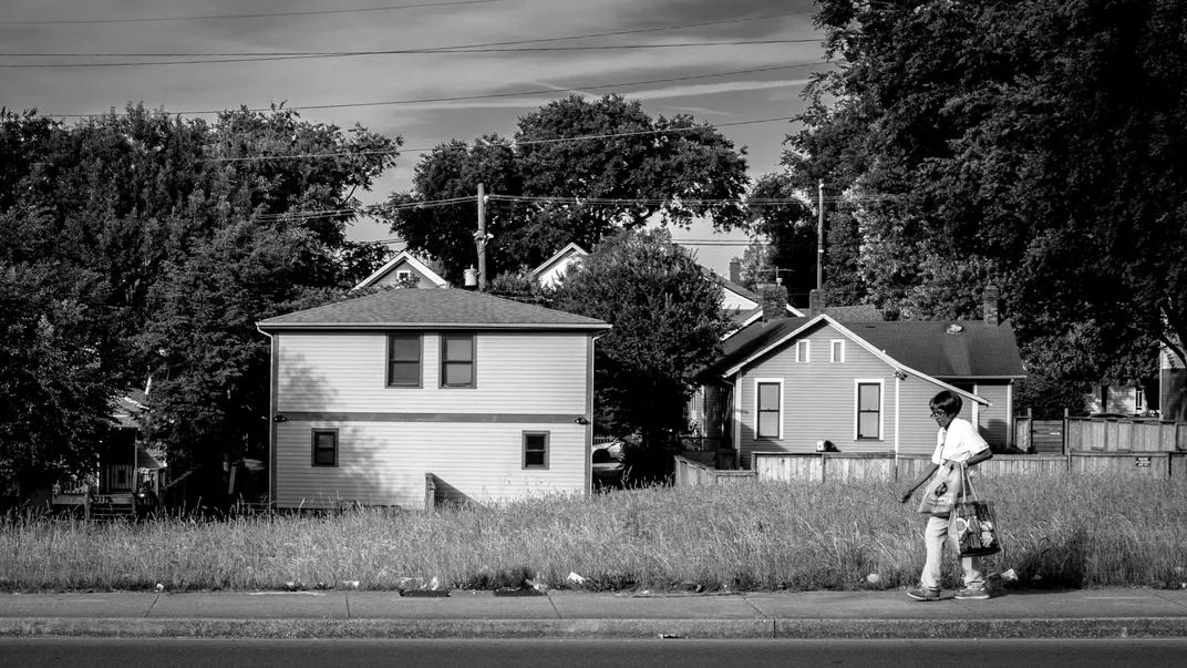 A black and white image of an older Black woman walking down the street