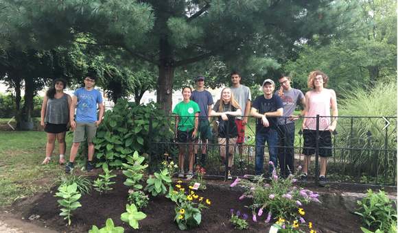 A group of young people stand in front of a pollinator garden in Lowell, MA