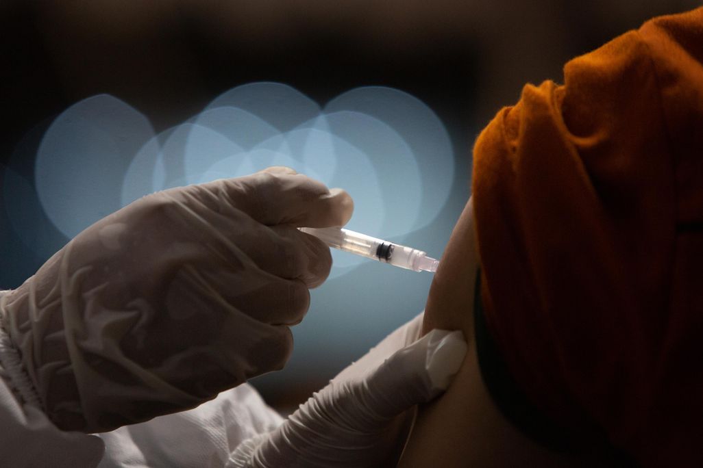 An Indonesian doctor injects a dose of Sinovac COVID-19 vaccine to a man's upper arm. 