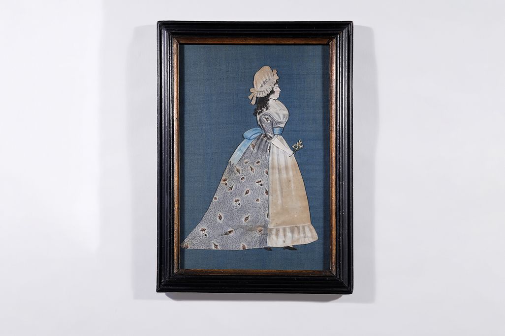 A vertical portrait of a woman in a full gown with a floral calico print on periwinkle; she holds a flower in one hand
