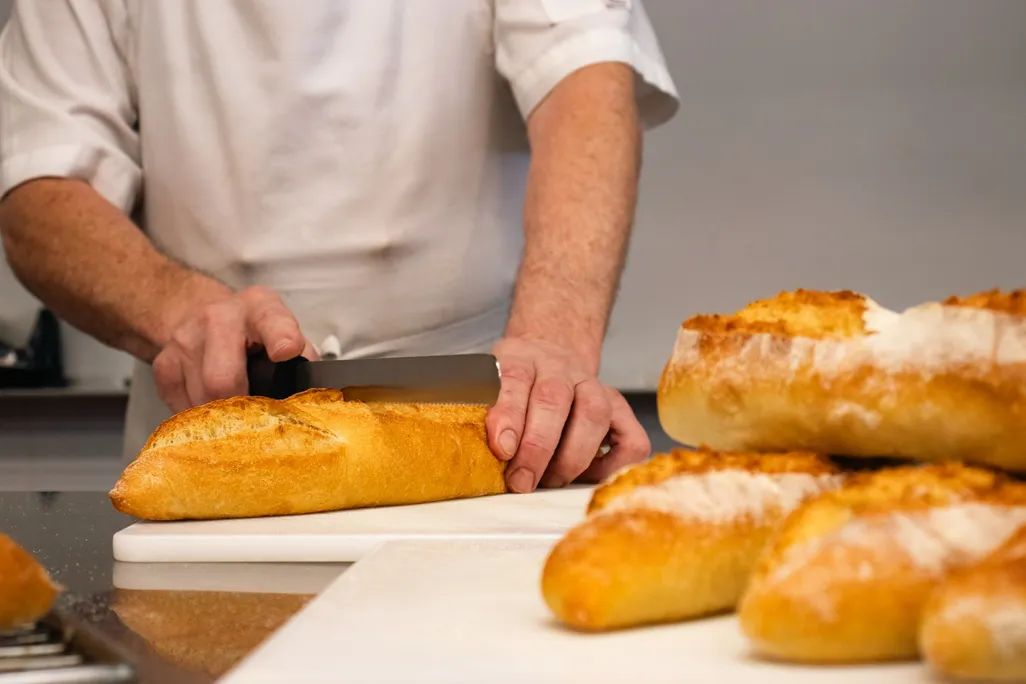 Chef cutting a loaf of bread with other loaves nearby